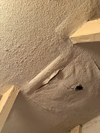 Damaged artex textured ceiling with a hole exposing the substrate — asbestos risk if disturbed